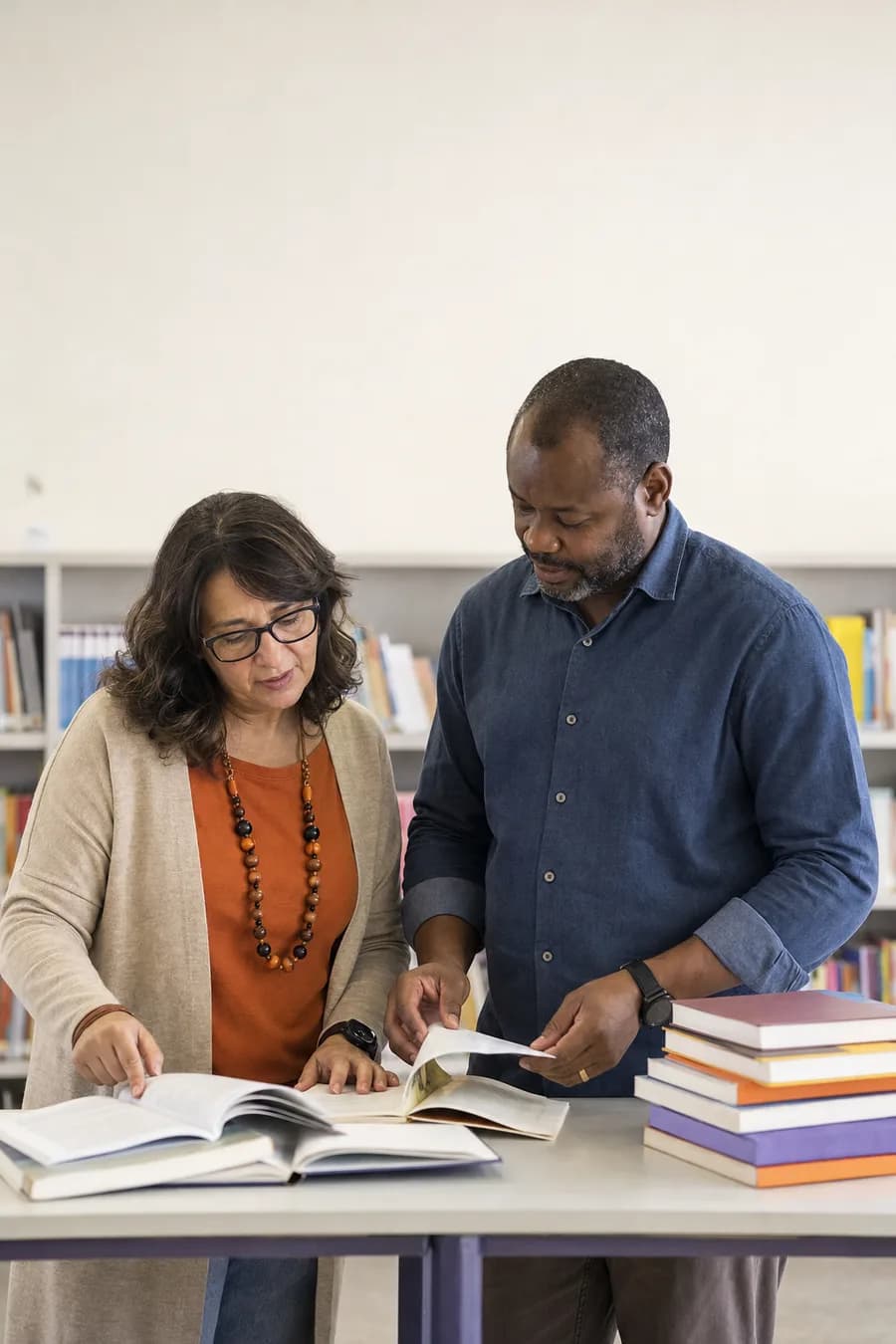Coordenadora da rede e diretor de escola examinam livros didáticos na biblioteca